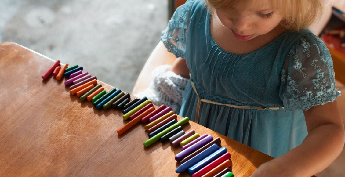طفلة شقراء تجلس بمفردها تلعب بالألوان وتعاني من النمط الظاهري للتوحد الواسع (Broad Autism Phenotype)