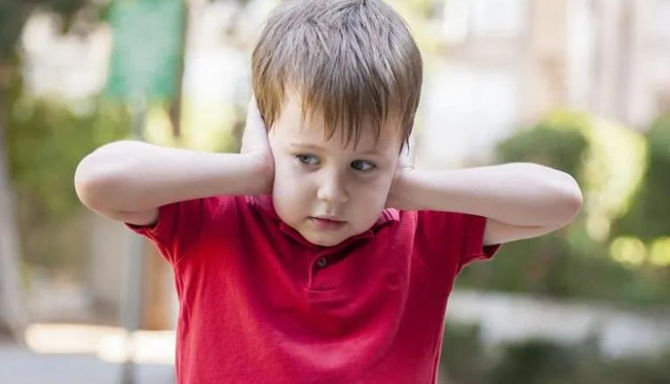 طفل صغير مصاب باضطراب طيف التوحد يضع يديه على أذنيه كي لا يسمع شيئاً كون ذلك من مسببات اضطراب التوحد