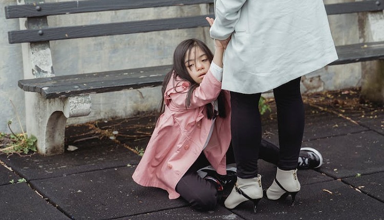 طفلة مصابة بالتوحد تجلس على الأرض منهارة لتعرضها للحمل الحسي الزائد وهي من طرق علاج التوحد عند المراهقين وبجانبها أمها.