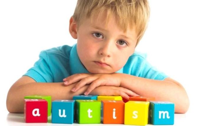 طفل أشقر يرتدي بلوزة زرقاء ويضع يديه على مجموعة مكعبات مكتوب عليها autism للدلالة على علامات التوحد 