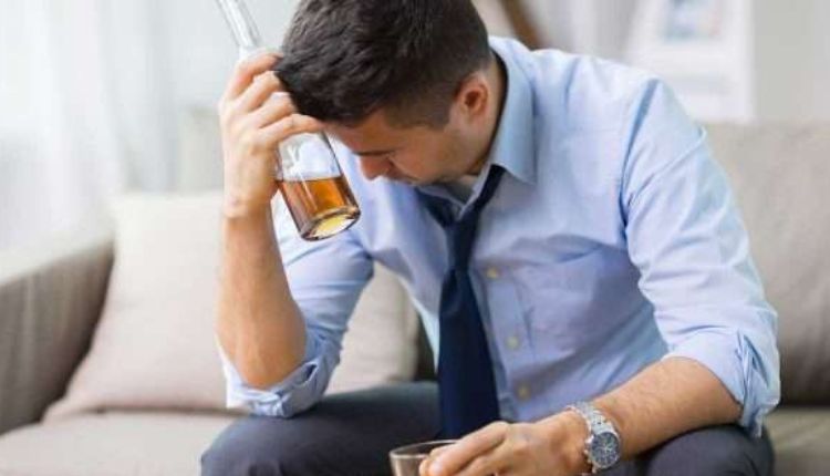 رجل جالس ويمسك بيده زجاجة كحول ويفرط بالشرب وهي أحد سمات اضطراب تعاطي الكحول