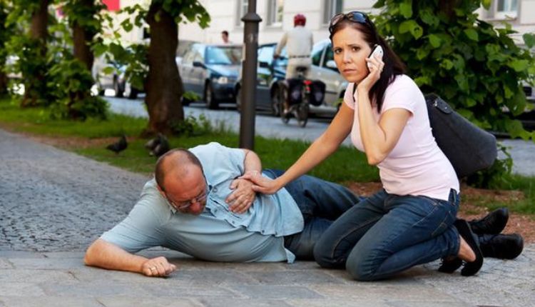 رجل على الأرض في الشارع يضع يده على قلبه وبجانبه ابنته تتصل بالإسعاف لبيان الآثار الجانبية لادمان الإيبوبروفين