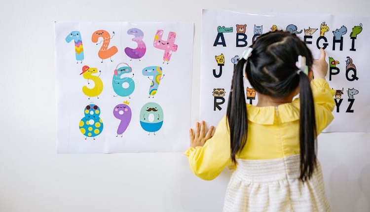 طفلة توحدية تقف أمام حائط عليها أرقام وحروف وتكتب هي أحد طرق تعليم الطفل التوحدي الخلفية بيضاء