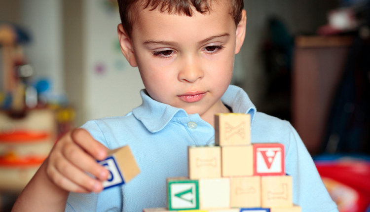 طفل صغير مصاب بالتوحد يلعب بالمكعبات حيث إن الجينات الوراثية للتوحد إحدى أبرز أسباب التوحد