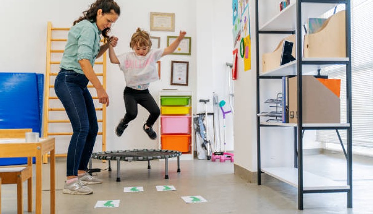 طفلة تقفز وبجانبها مدربة ADHD تمسك بيدها الخلفية بيضاء كيفية ايجاد متخصص بفرط الحركة 