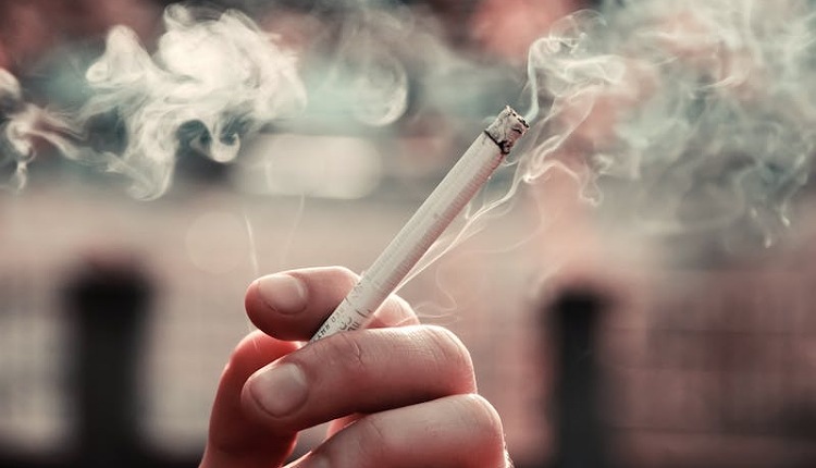 سيجارة يخرج منها دخان يمسكها شخص بيده لا يعرف كيفية الإقلاع عن الإدمان الخلفية ضباب متعددة الألوان 