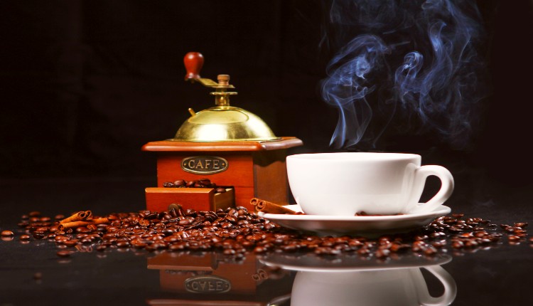 مطحنة القهوة وبجانيها فنجان من القهوة يتصاعد منه البخار لمعرفة ماذا يفعل الكافيين في الجسم