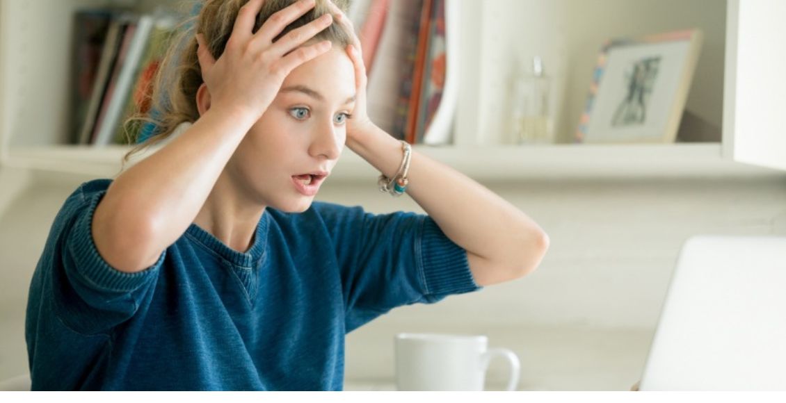 فتاة تجلس في مكتب وتضع يدها على رأسها لتوضيح أسباب نوبات القلق Anxiety Attacks Cause