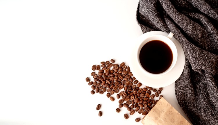 فنجان القهوة بجانب حبوبها غير المطحونة وأهمية التقليل من القهوة
