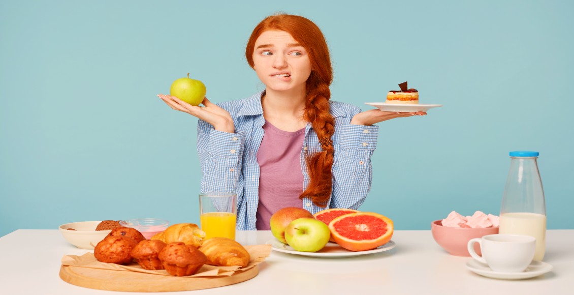 فتاة تمسك بيد قطعة من الحلوى واليد الأخرى تفاح لتوضيح أهمية الطعام الصحي والقلق anxiety healthy diet relationship
