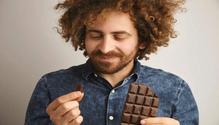 رجل يبتسم وهو يمسك قالب من الشيكولاته الداكنة يوضح نوع من أنواع الأطعمة يحد من التوتر